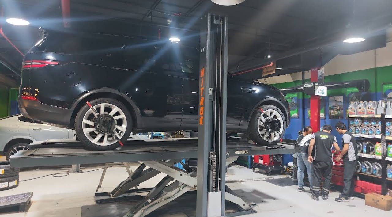 Vehicle on workshop hydraulic lift undergoing laser wheel alignment